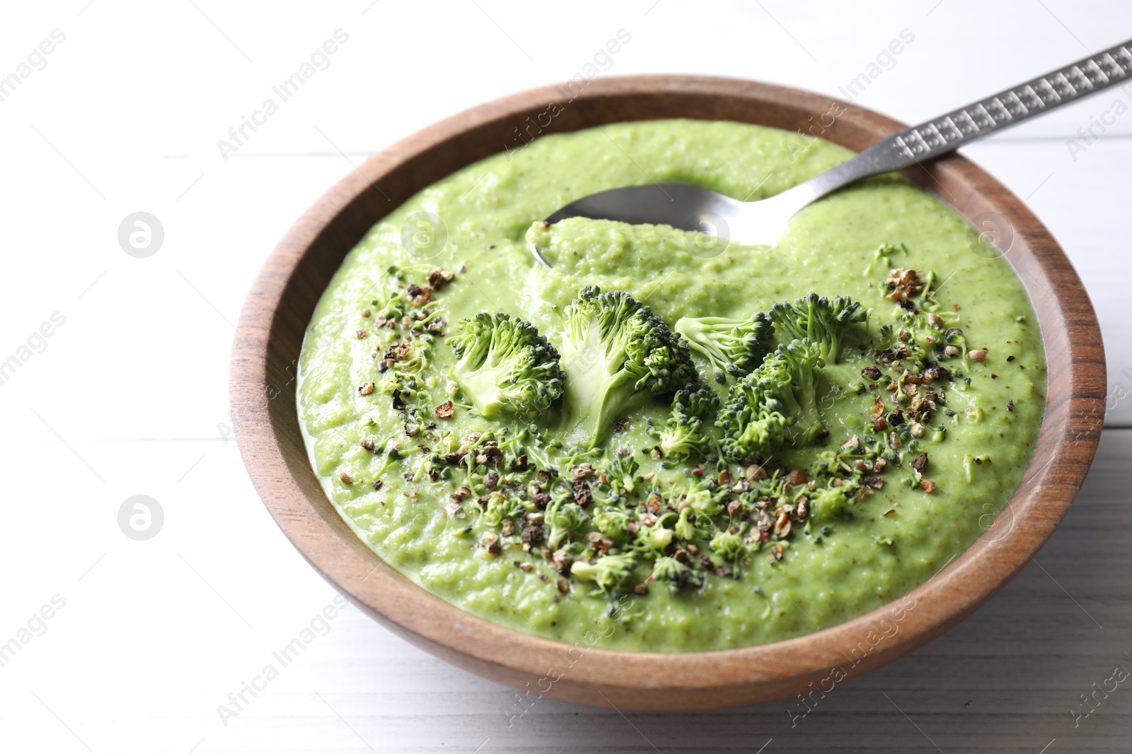 Photo of Delicious broccoli cream soup and spoon in bowl on white wooden table, closeup