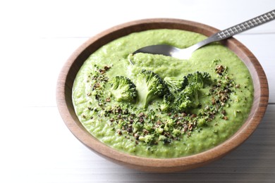 Photo of Delicious broccoli cream soup and spoon in bowl on white wooden table, closeup