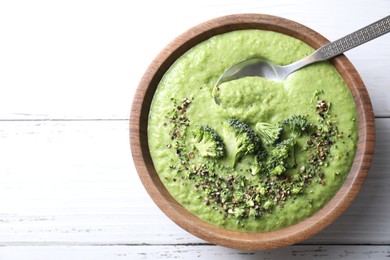 Photo of Delicious broccoli cream soup and spoon in bowl on white wooden table, top view. Space for text