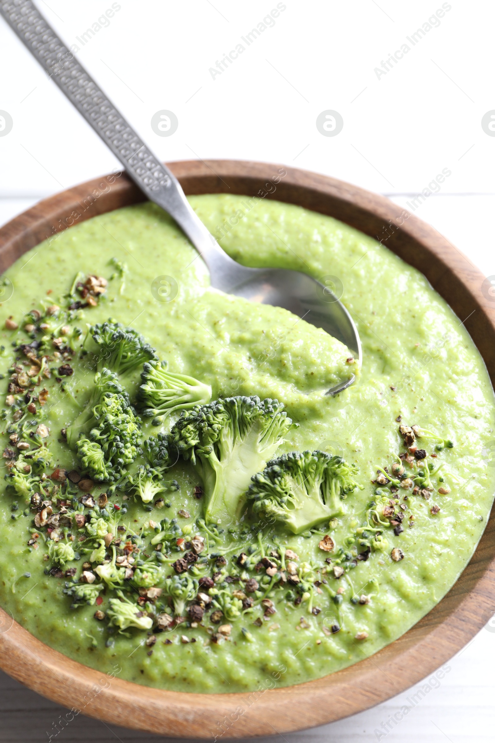 Photo of Delicious broccoli cream soup and spoon in bowl on white wooden table, closeup