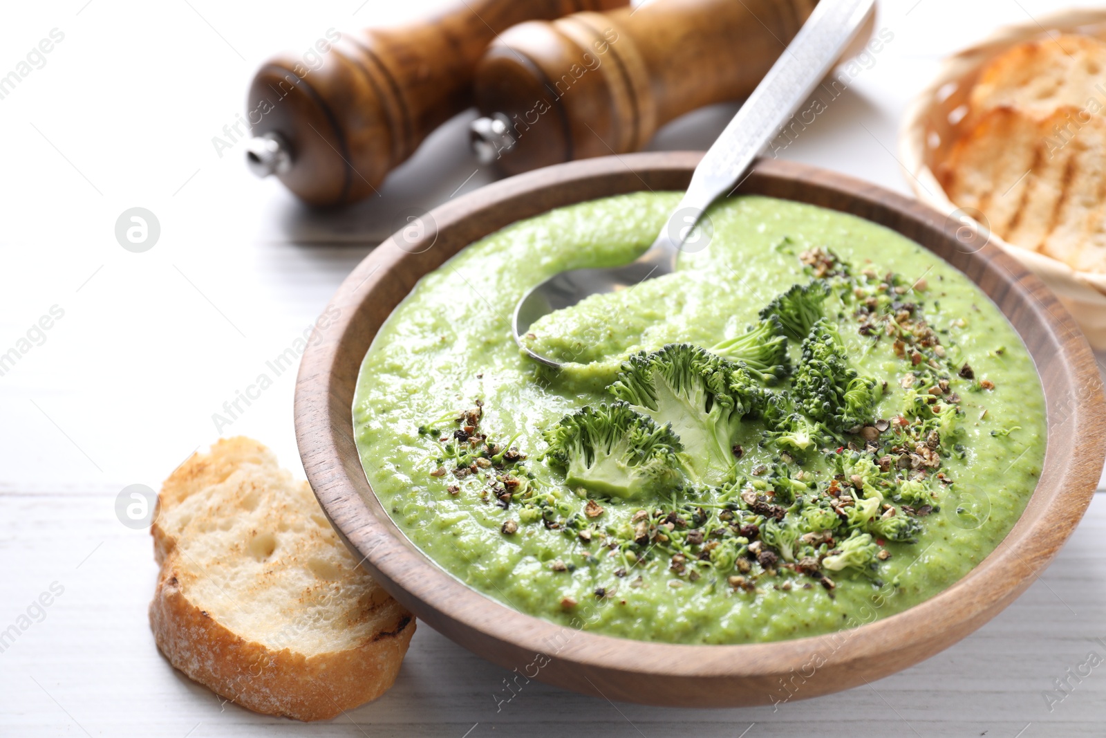 Photo of Delicious broccoli cream soup served on white wooden table, closeup