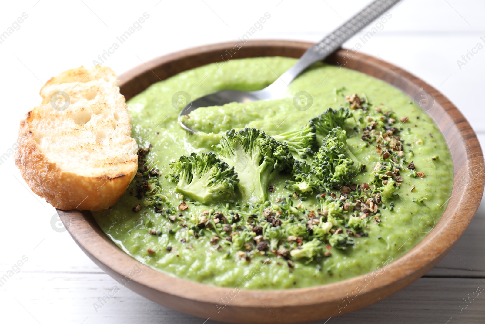 Photo of Delicious broccoli cream soup served on white wooden table, closeup