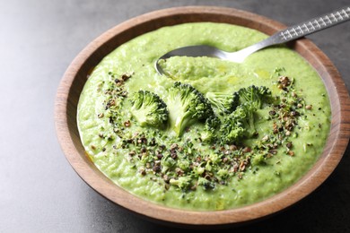 Photo of Delicious broccoli cream soup in bowl and spoon on grey table, closeup