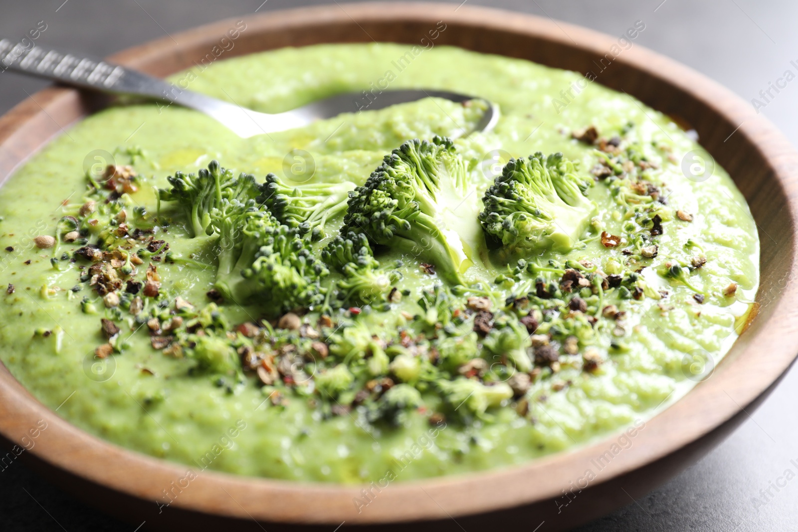 Photo of Delicious broccoli cream soup in bowl and spoon on grey table, closeup