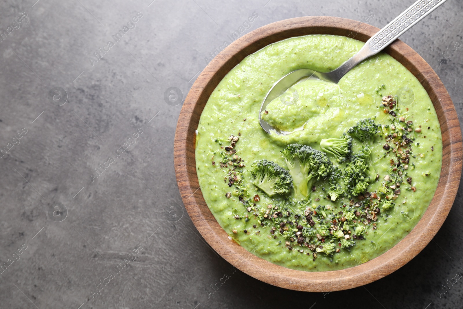 Photo of Delicious broccoli cream soup and spoon in bowl on grey table, top view. Space for text