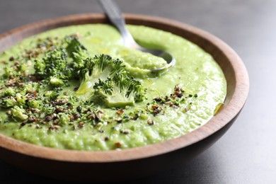 Photo of Delicious broccoli cream soup in bowl and spoon on grey table, closeup