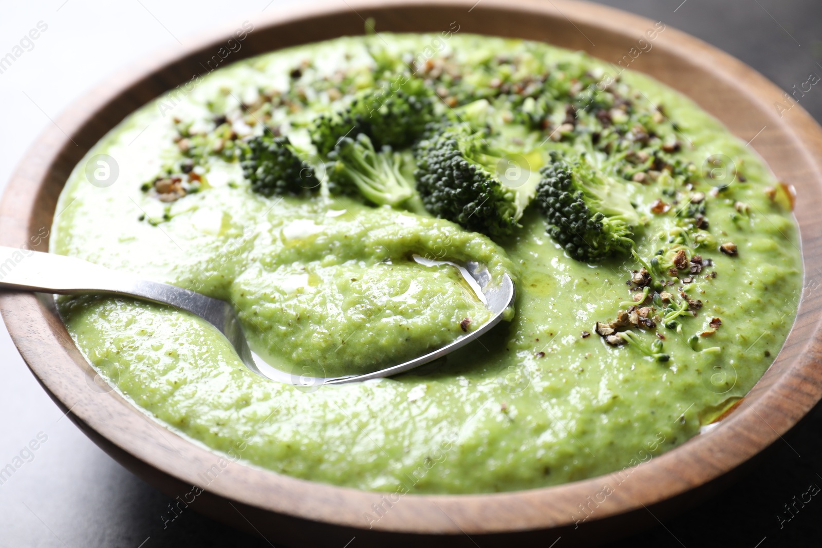 Photo of Delicious broccoli cream soup in bowl and spoon on grey table, closeup