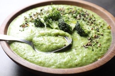 Photo of Delicious broccoli cream soup in bowl and spoon on grey table, closeup