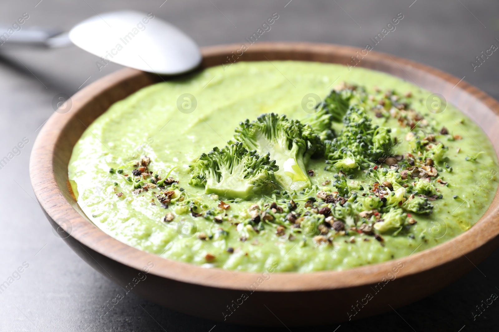 Photo of Delicious broccoli cream soup in bowl and spoon on grey table, closeup