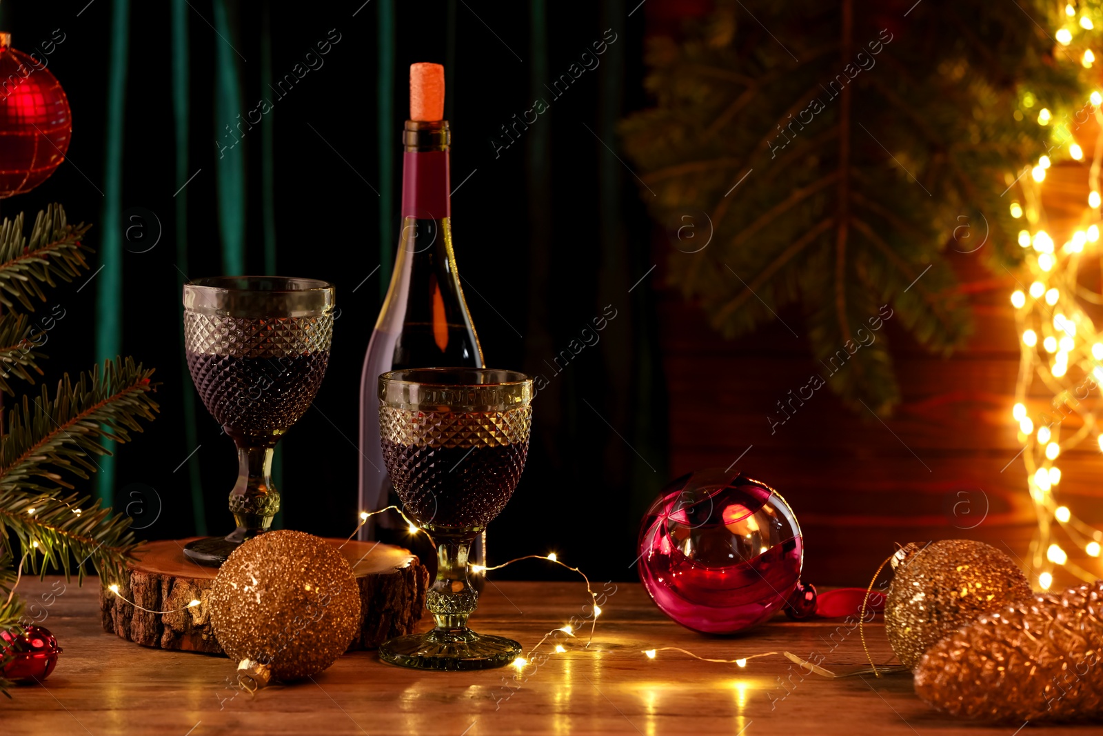 Photo of Red wine and beautiful Christmas decor on wooden table against blurred festive lights. Space for text