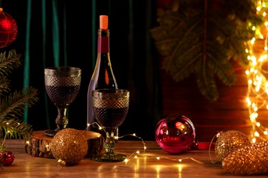 Photo of Red wine and beautiful Christmas decor on wooden table against blurred festive lights. Space for text