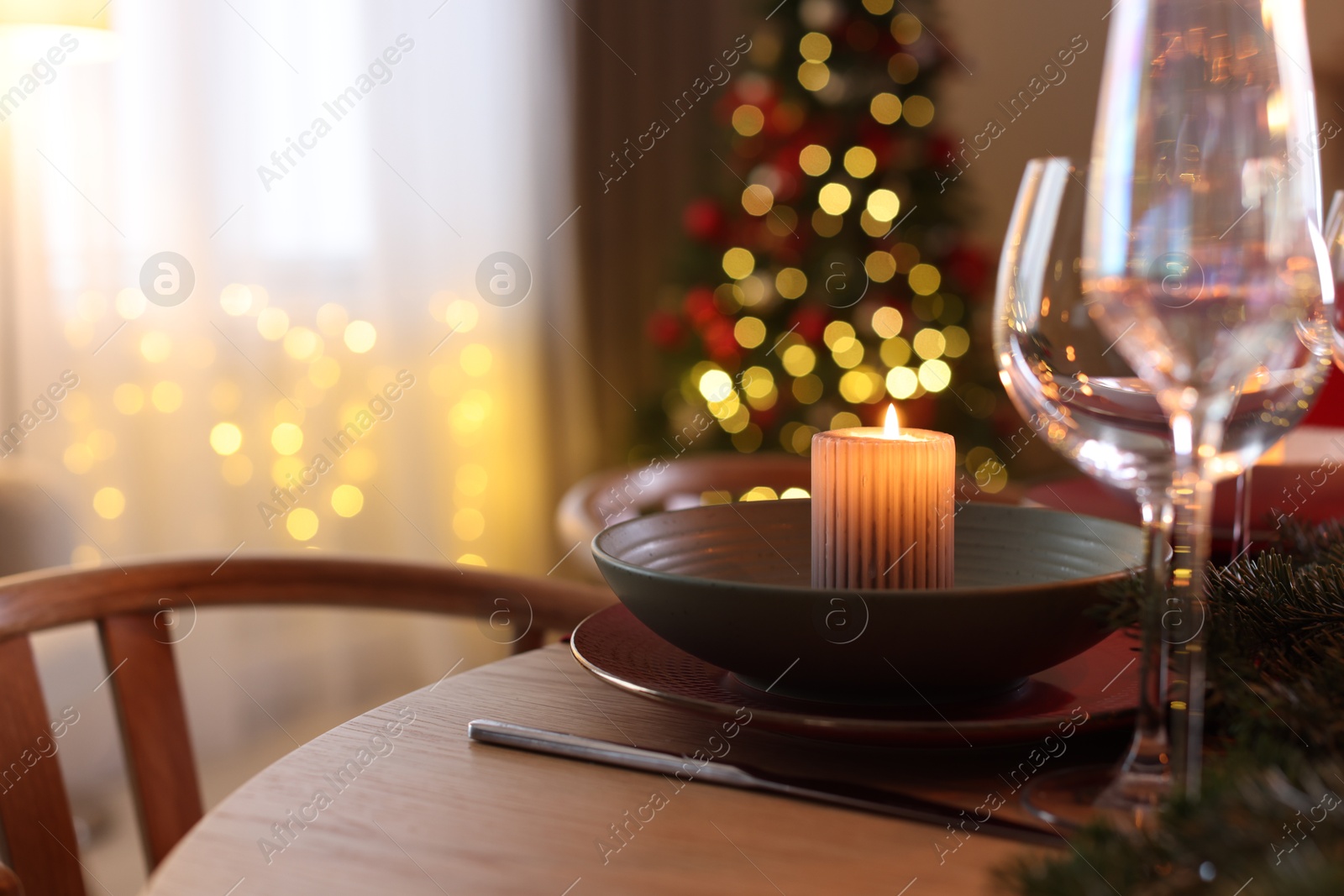 Photo of Beautiful dishware with burning candle on table against blurred Christmas lights, closeup