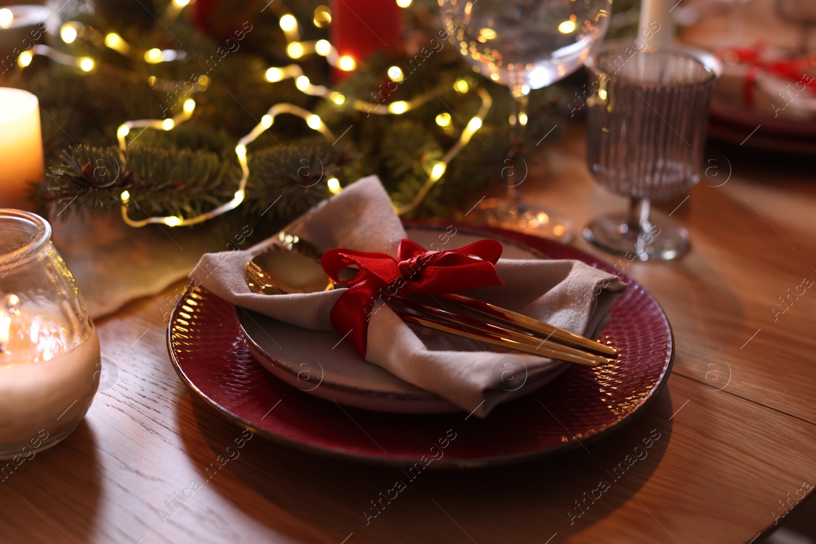 Photo of Beautiful dishware and Christmas lights on wooden table indoors, closeup