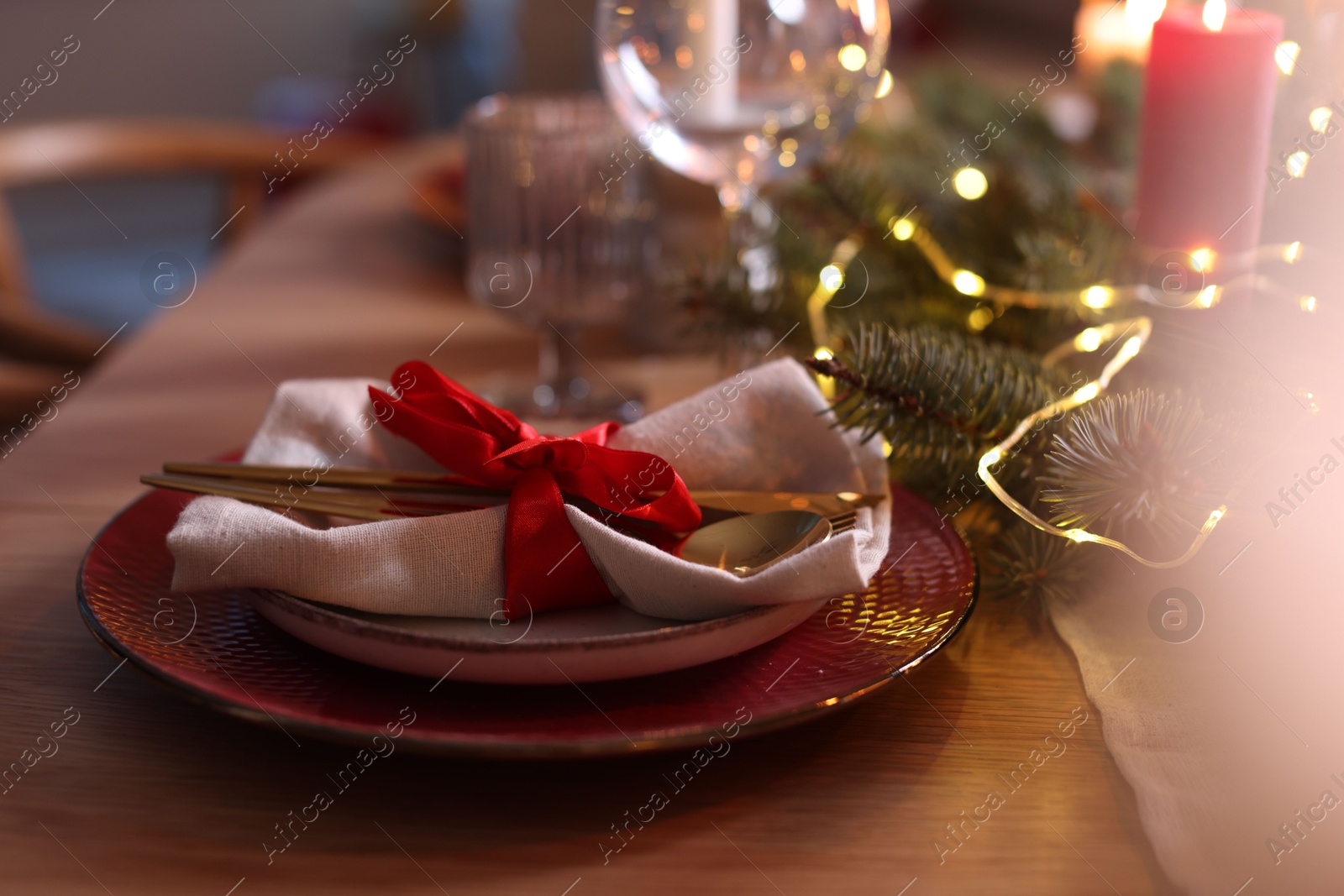 Photo of Beautiful dishware and Christmas lights on wooden table indoors, closeup