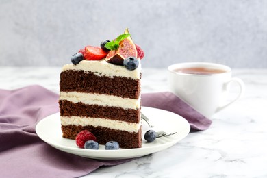 Photo of Piece of delicious chocolate sponge cake with berries and tea on white table, closeup