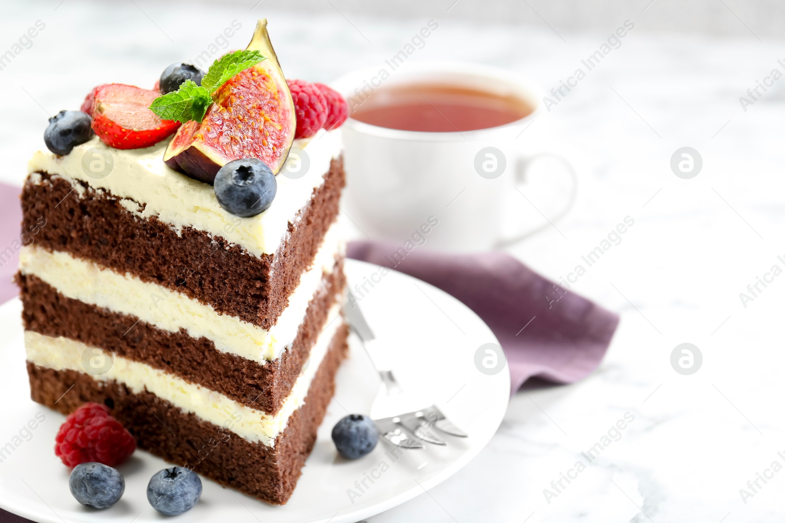 Photo of Piece of delicious chocolate sponge cake with berries and tea on white table, closeup