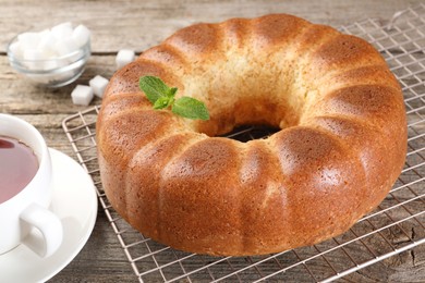 Photo of Freshly baked sponge cake, sugar cubes and tea on wooden table, closeup