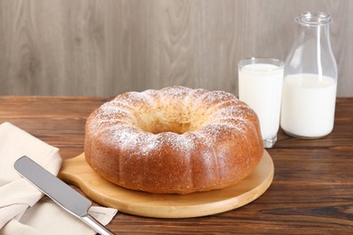 Photo of Freshly baked sponge cake, knife and milk on wooden table