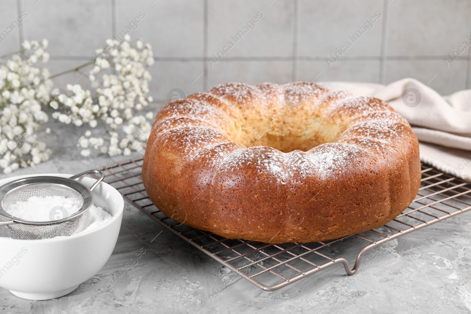 Photo of Freshly baked sponge cake with powdered sugar and flowers on grey table, closeup