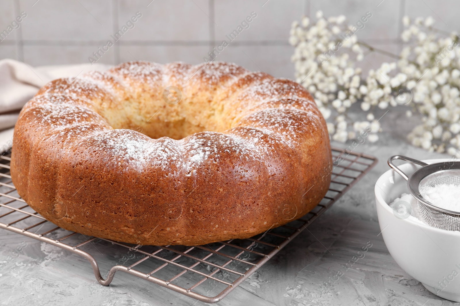 Photo of Freshly baked sponge cake with powdered sugar and flowers on grey table, closeup