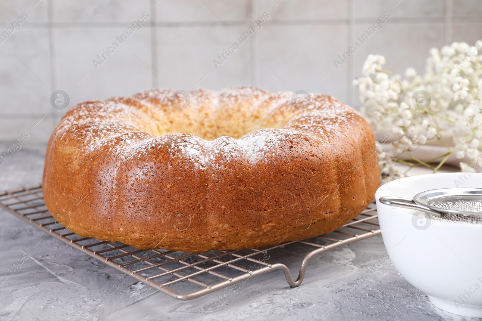 Photo of Freshly baked sponge cake with powdered sugar and flowers on grey table, closeup