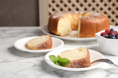 Photo of Freshly baked sponge cake, mint and berries on white marble table, closeup