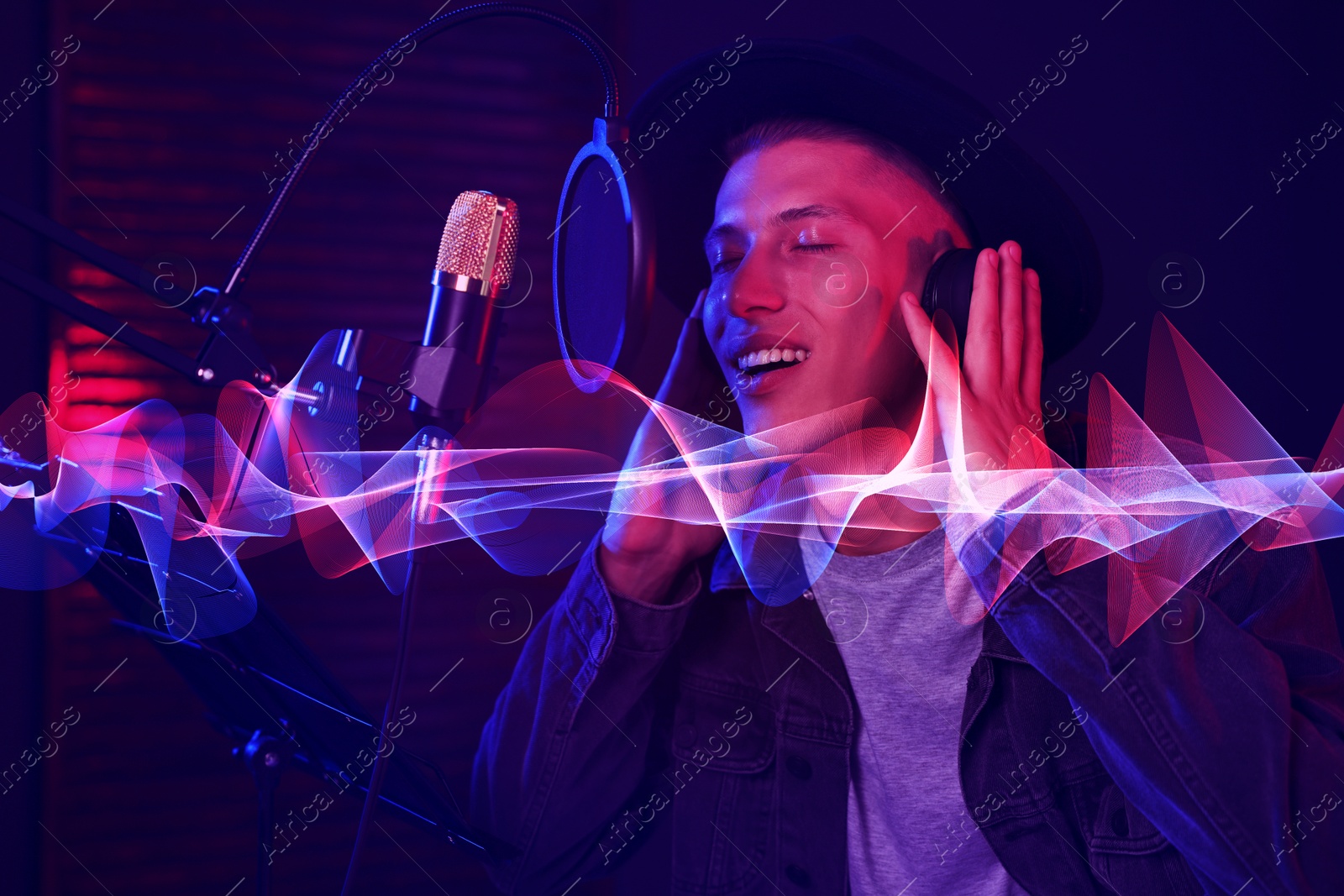 Image of Vocalist with headphones singing into microphone in professional record studio. Sound waves