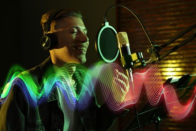 Image of Vocalist with headphones singing into microphone in professional record studio. Sound waves