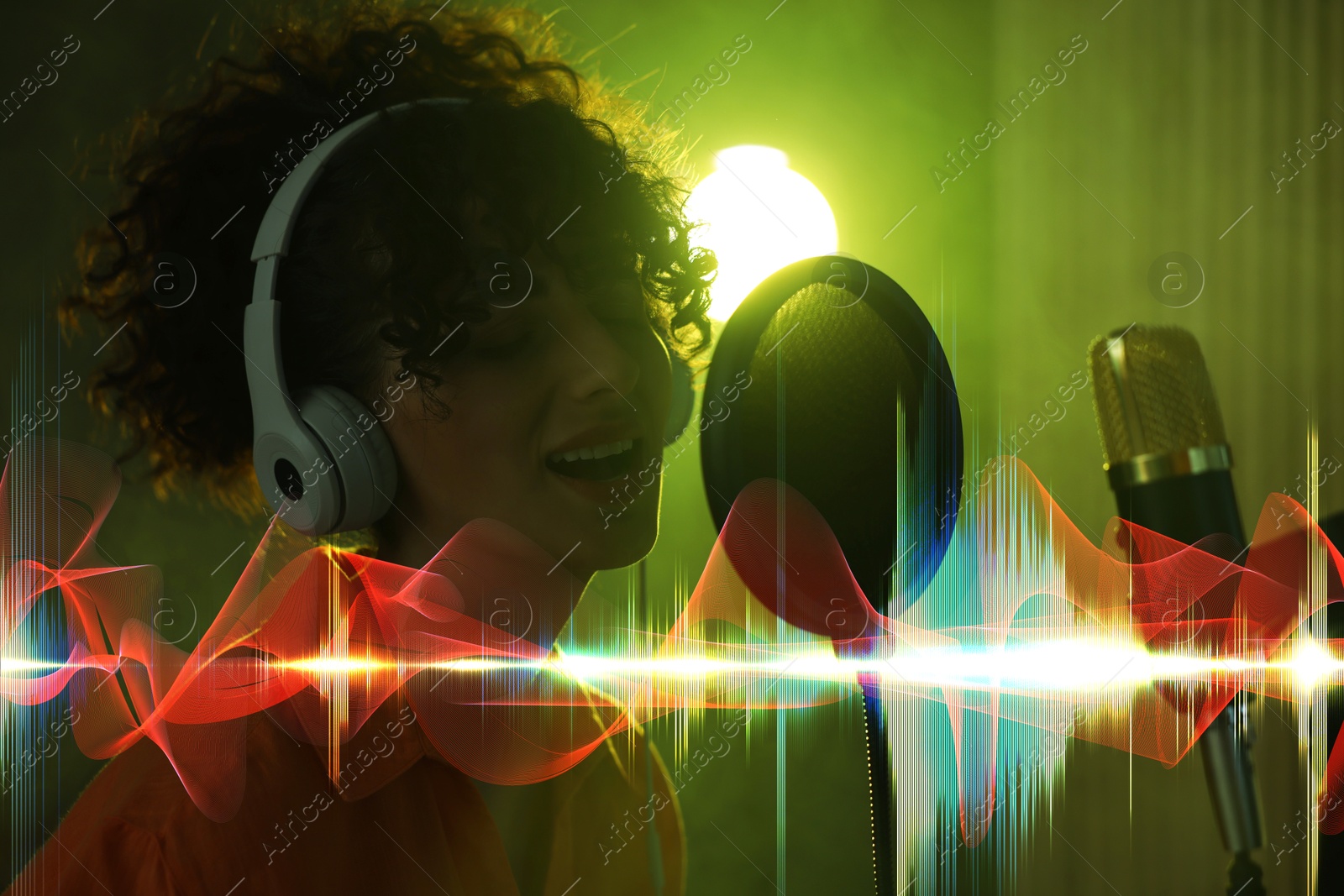 Image of Vocalist with headphones singing into microphone in professional record studio. Sound waves