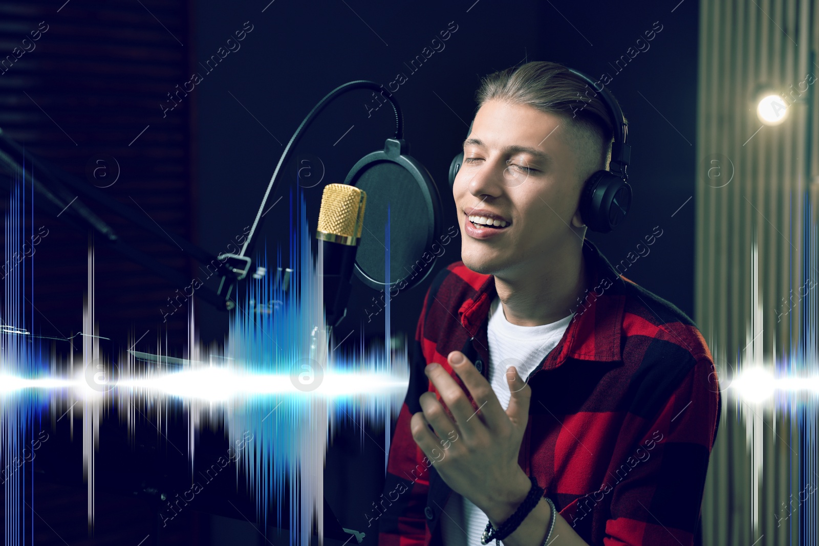 Image of Vocalist with headphones singing into microphone in professional record studio. Sound waves