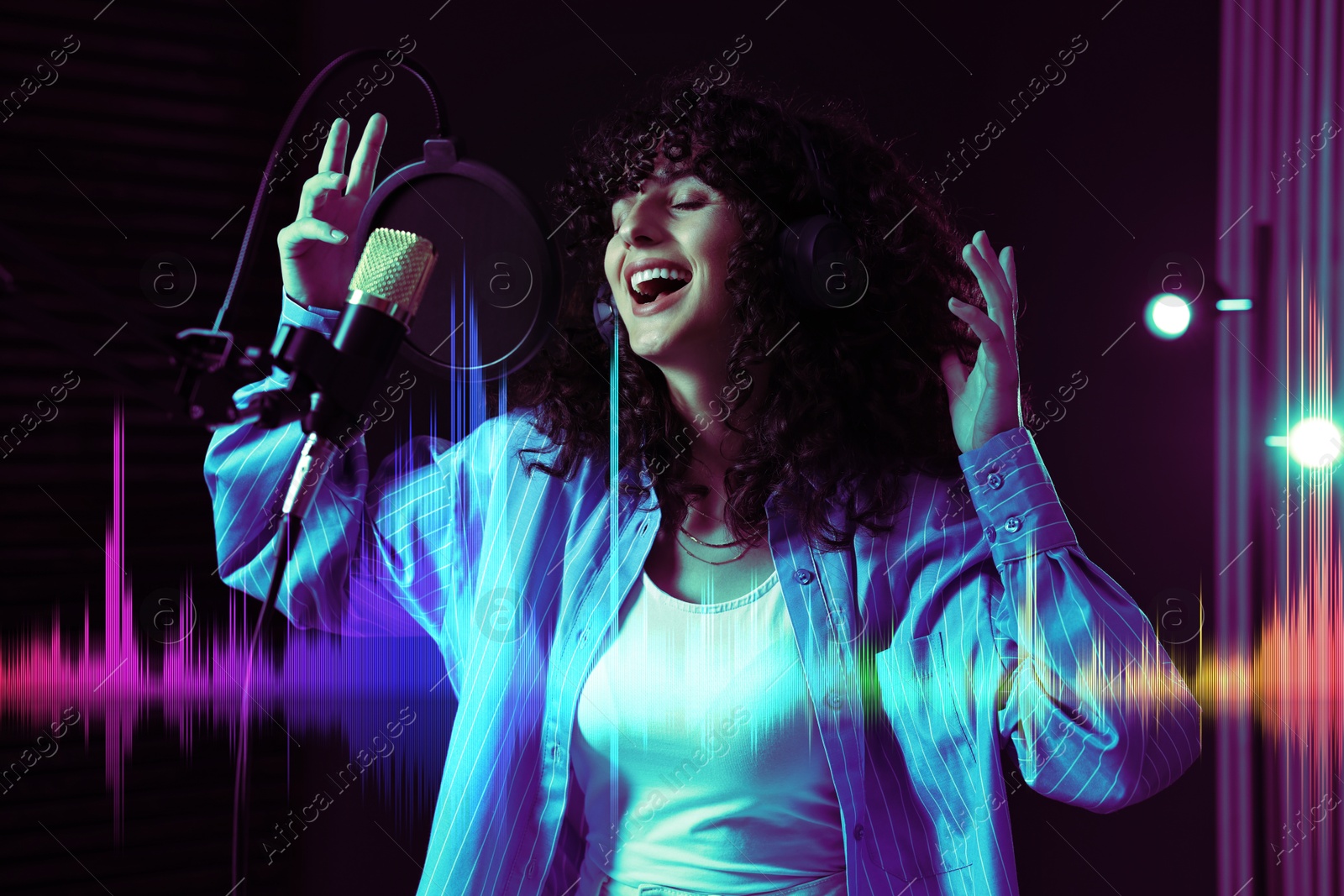 Image of Vocalist with headphones singing into microphone in professional record studio. Sound waves