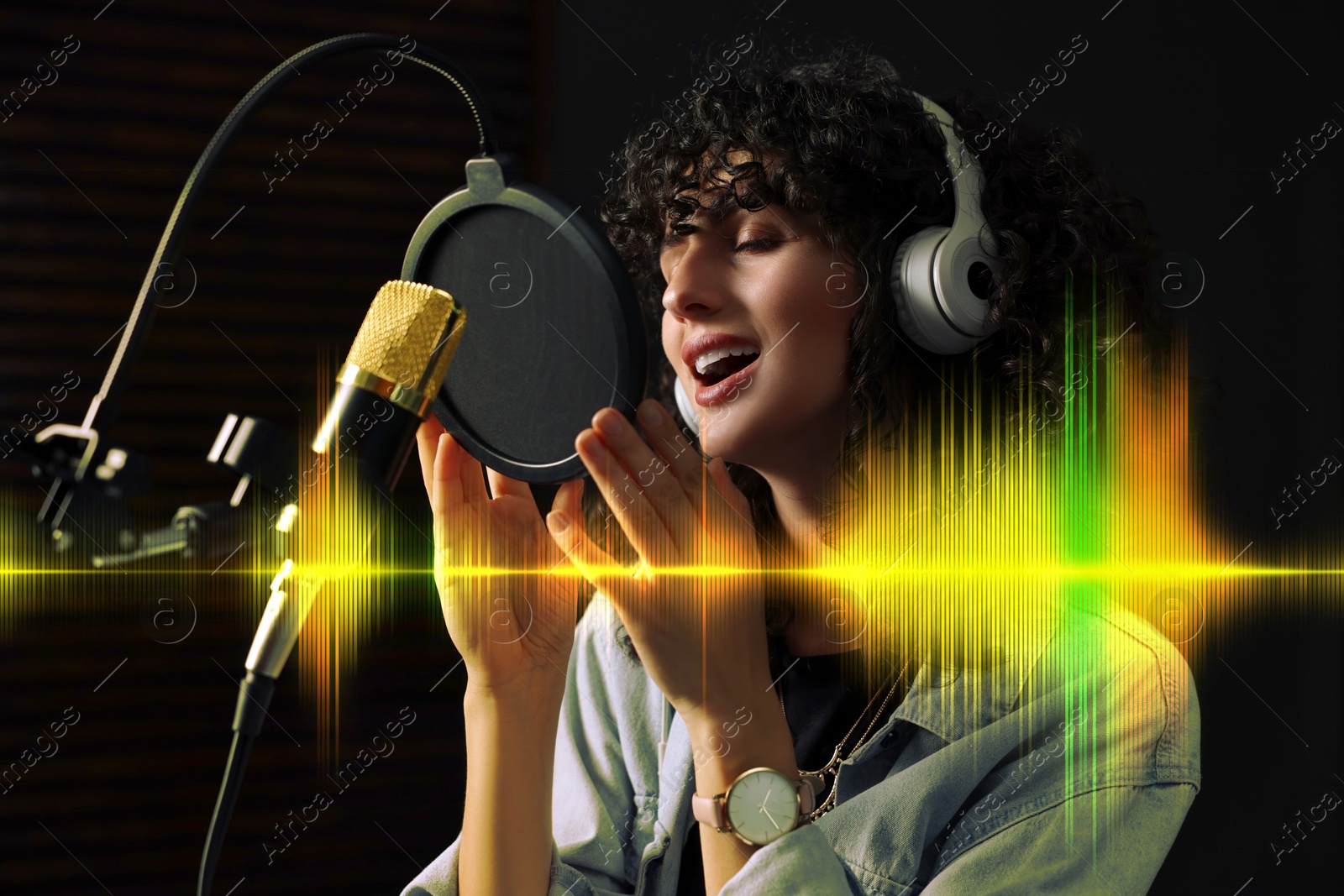 Image of Vocalist with headphones singing into microphone in professional record studio. Sound waves