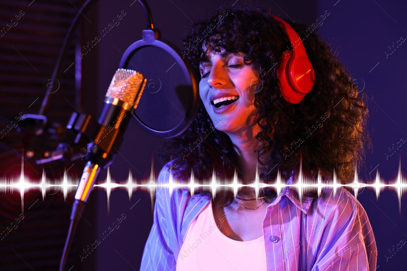 Image of Vocalist with headphones singing into microphone in professional record studio. Sound waves