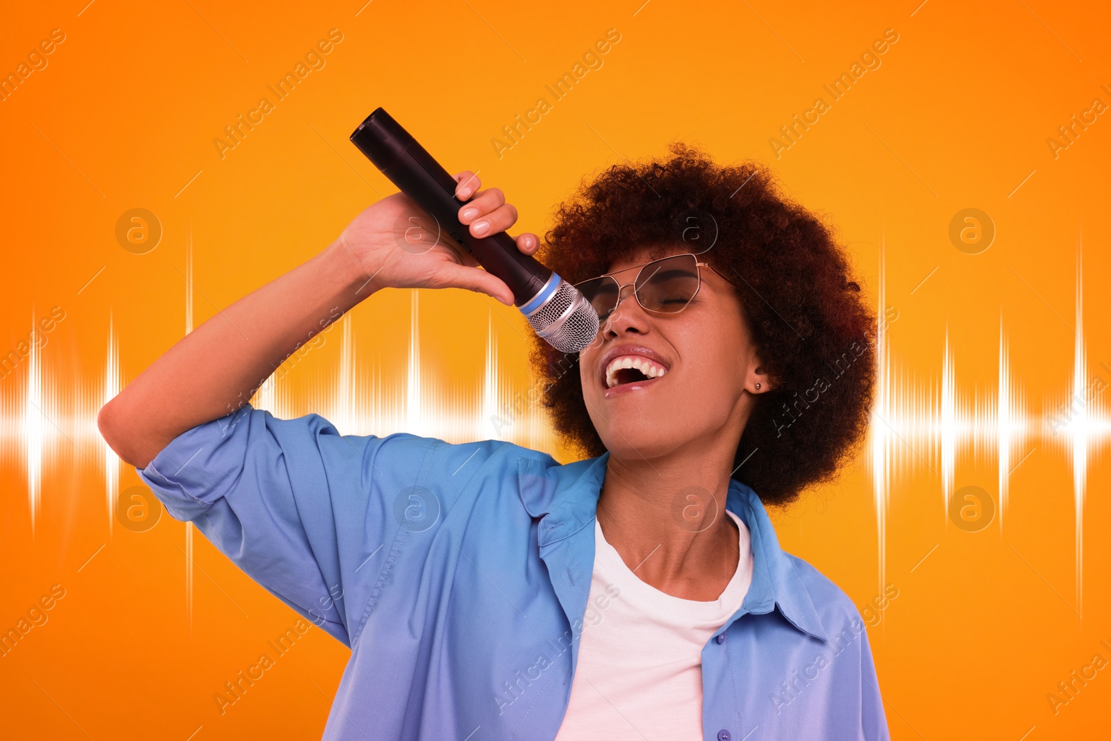 Image of Curly young woman in sunglasses with microphone singing on orange background. Sound waves