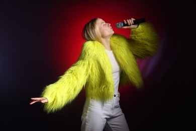 Photo of Talented singer in faux fur performing on dark background with red light