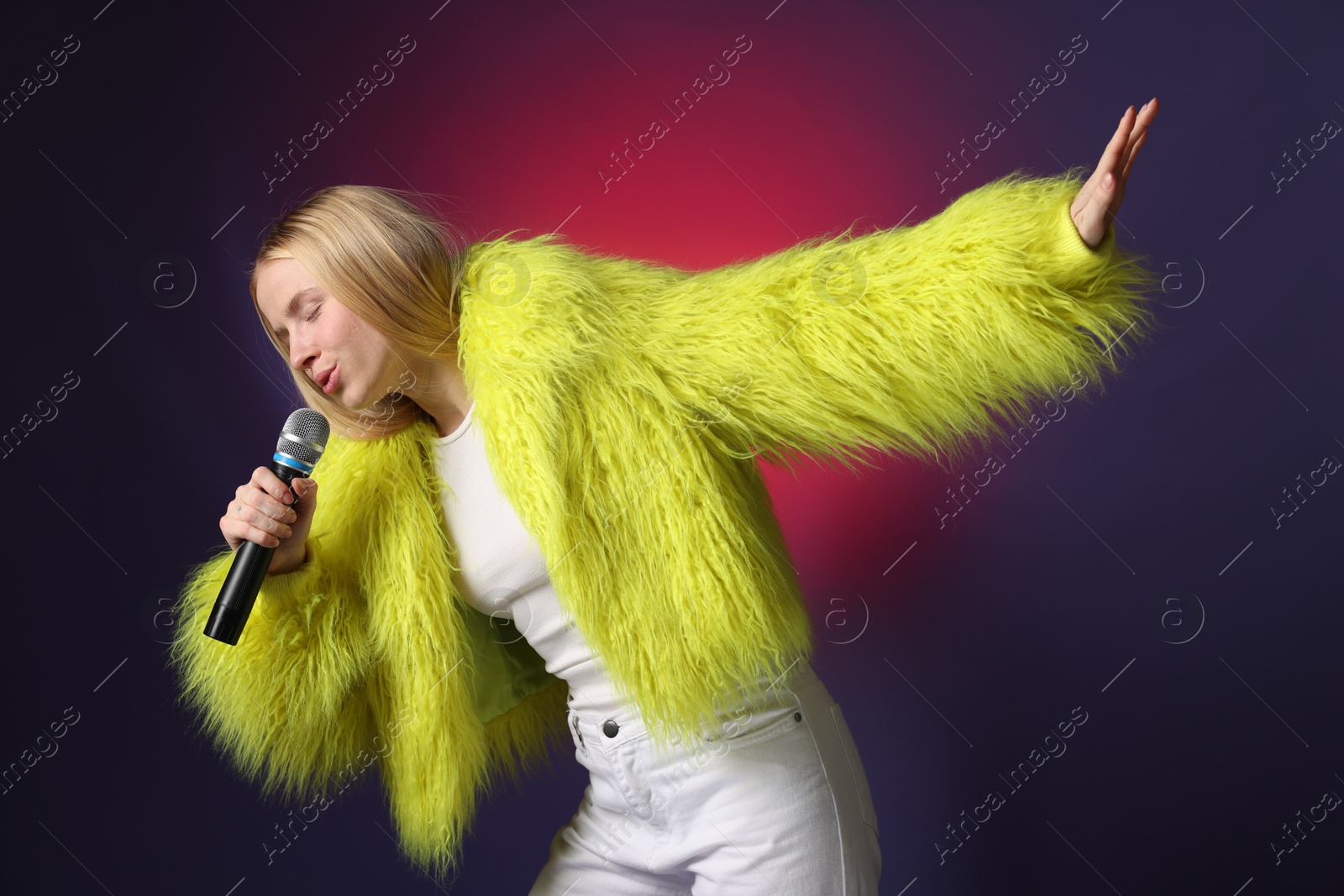 Photo of Talented singer in faux fur performing on dark background with pink light