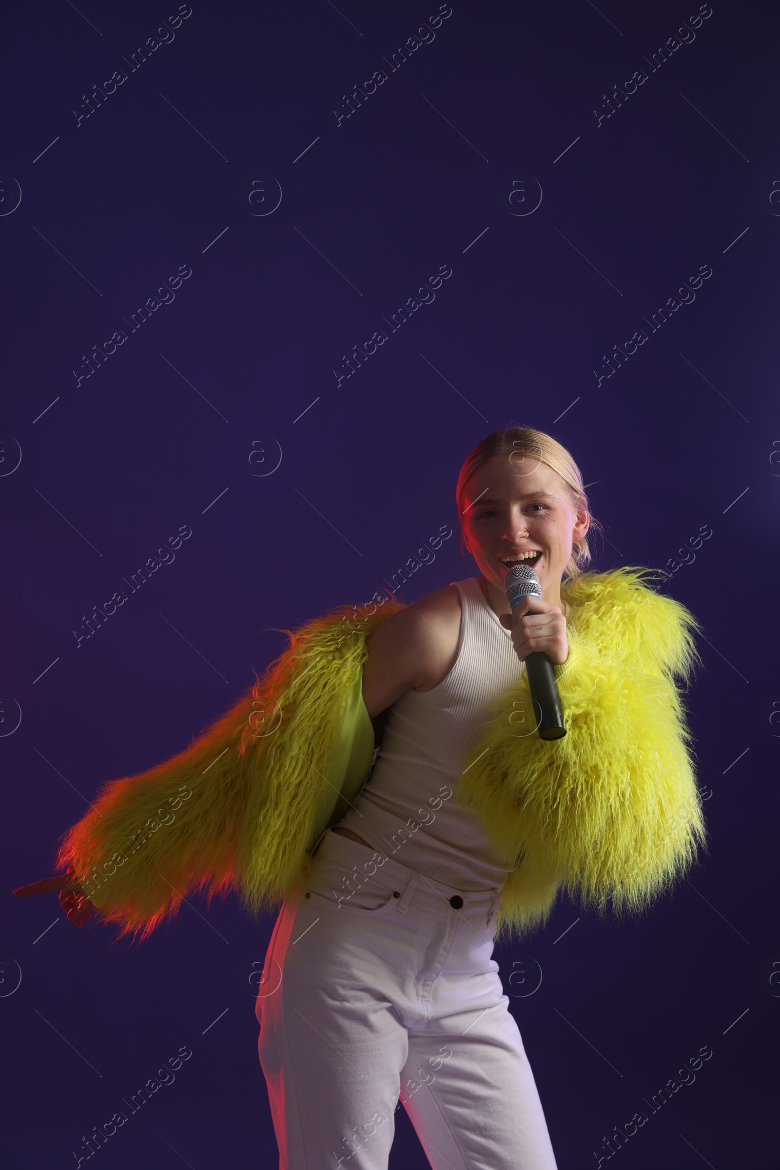 Photo of Talented singer in bright faux fur coat performing on purple background. Space for text