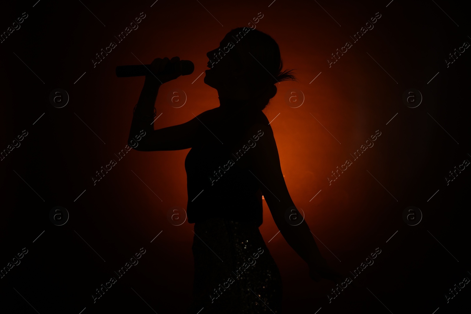 Photo of Silhouette of woman singing on dark background with color light