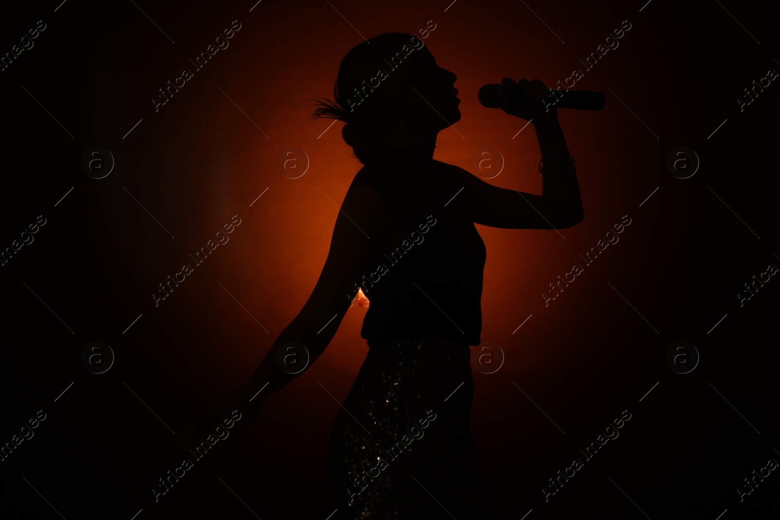 Photo of Silhouette of woman singing on dark background with color light