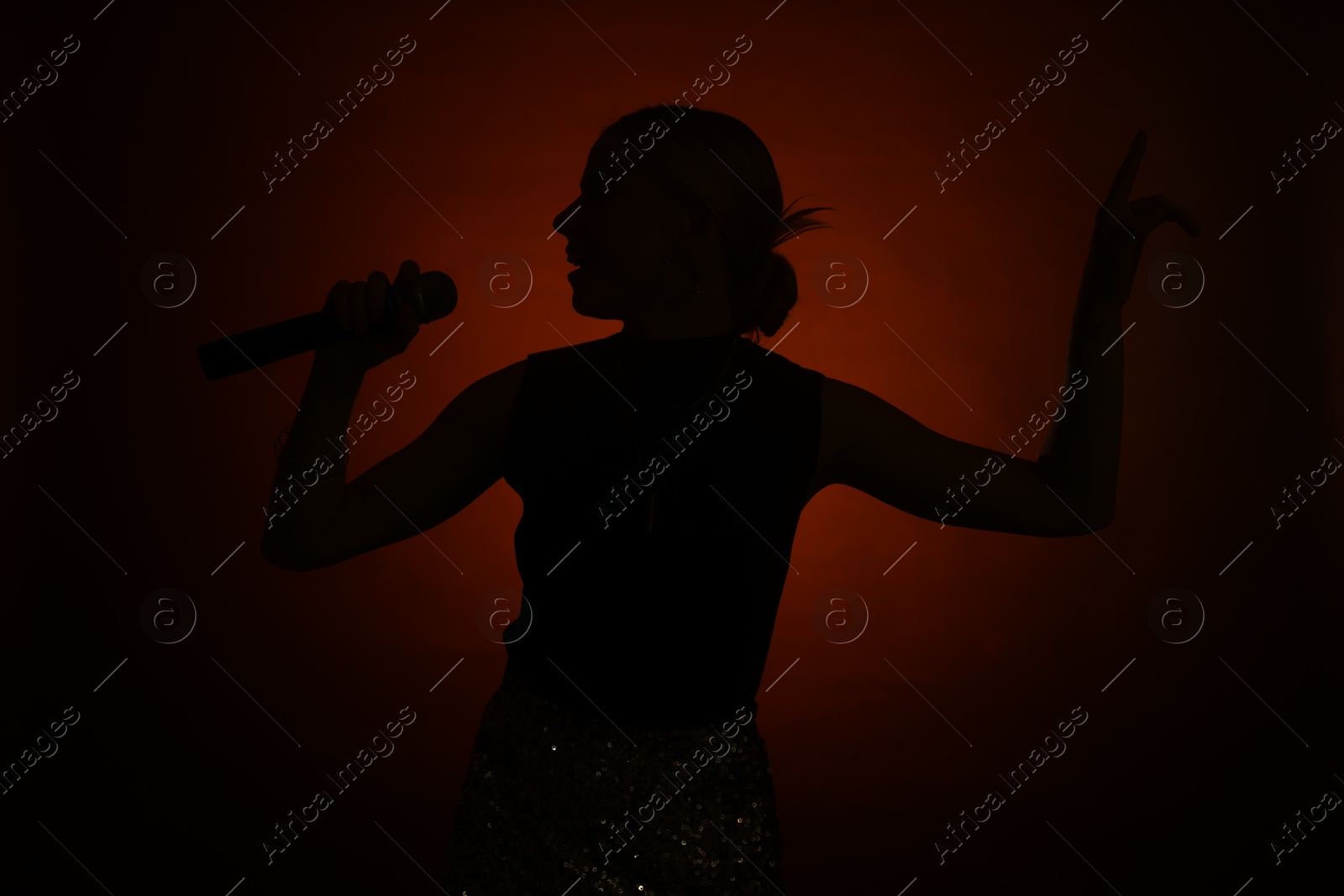 Photo of Silhouette of woman singing on dark background with color light