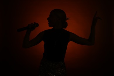 Photo of Silhouette of woman singing on dark background with color light