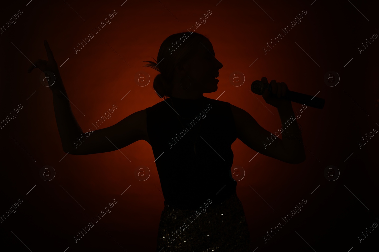 Photo of Silhouette of woman singing on dark background with color light