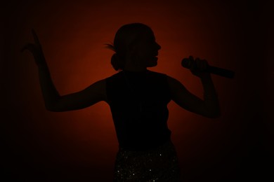 Photo of Silhouette of woman singing on dark background with color light