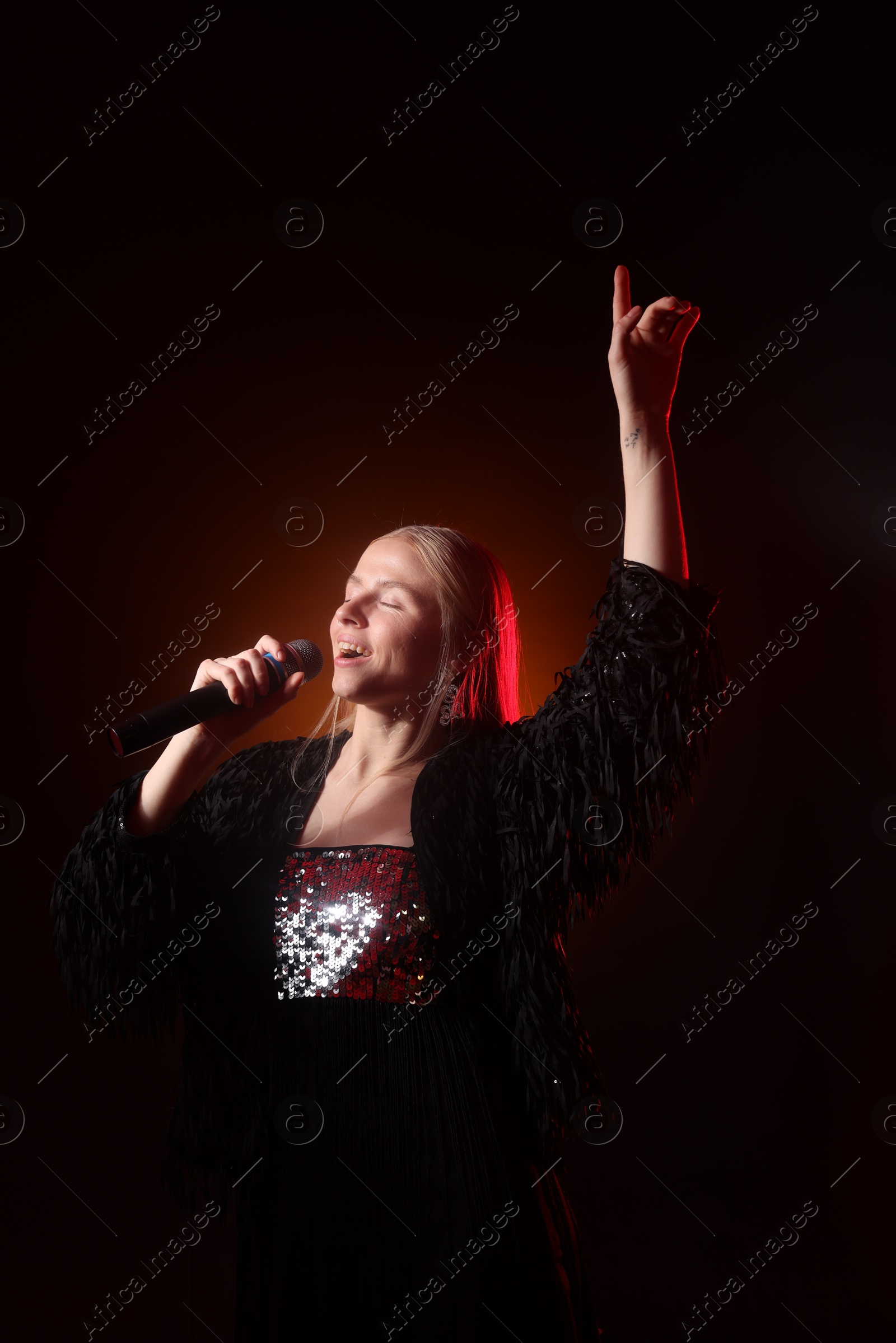 Photo of Beautiful singer performing on dark background with orange light