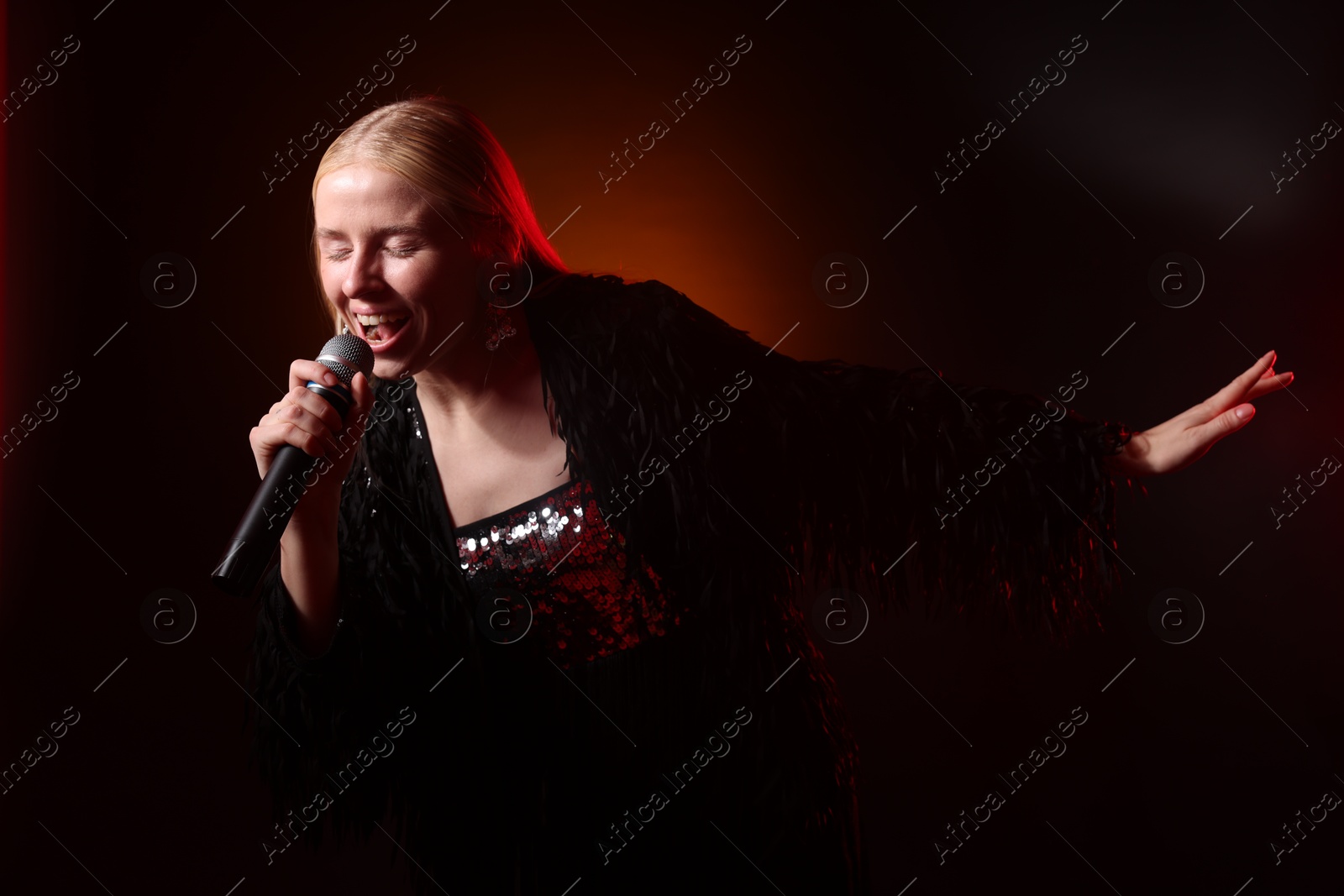 Photo of Beautiful singer performing on dark background with orange light