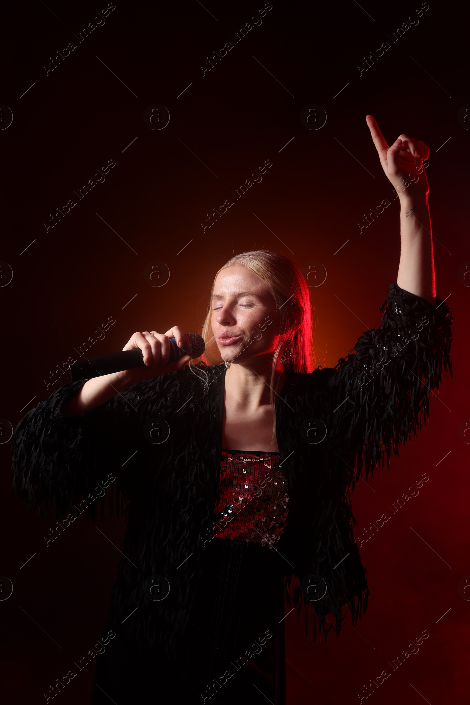 Photo of Beautiful singer performing on dark background with orange light