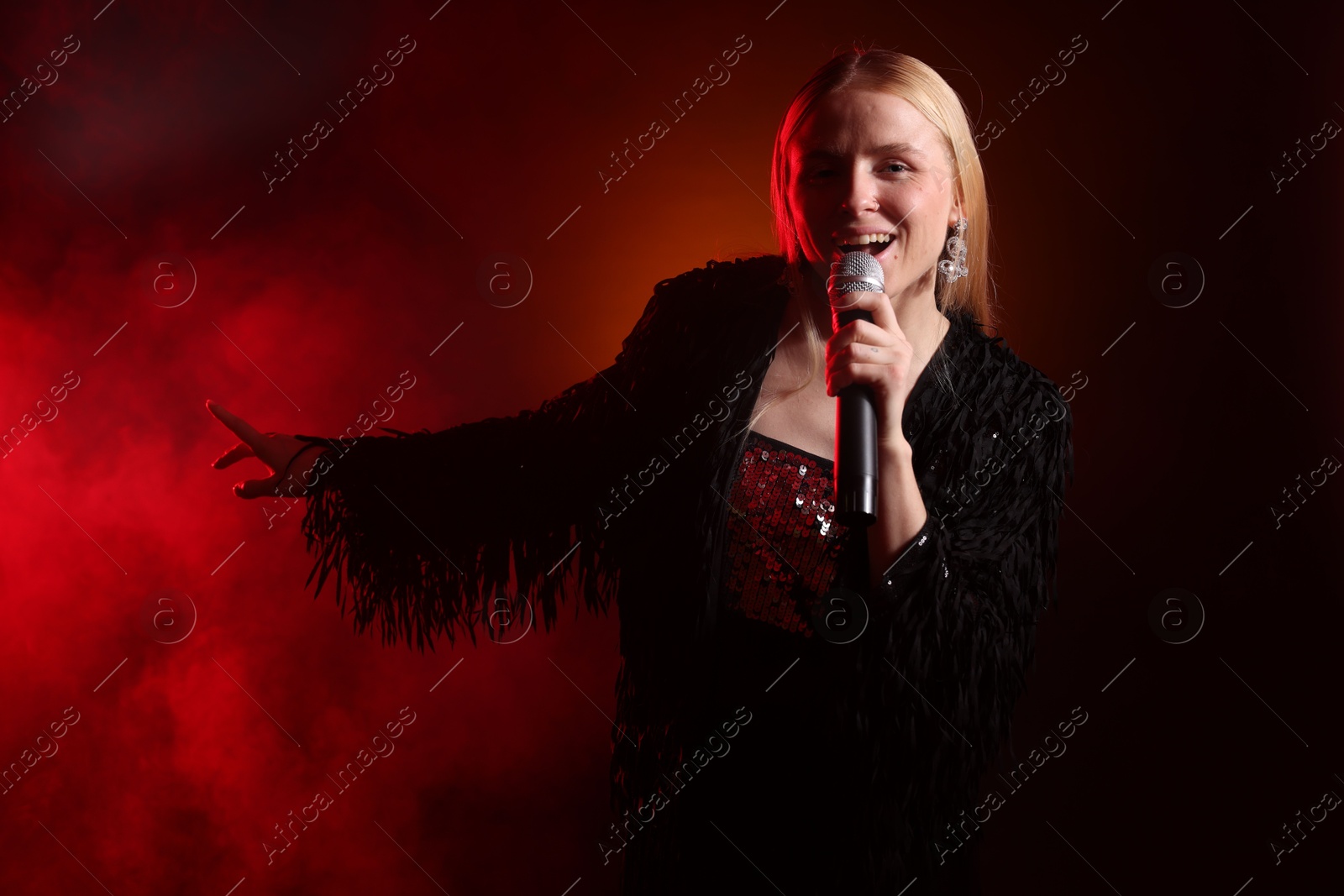 Photo of Beautiful singer performing on dark background with red light and smoke