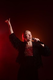 Photo of Beautiful singer performing on dark background with orange light