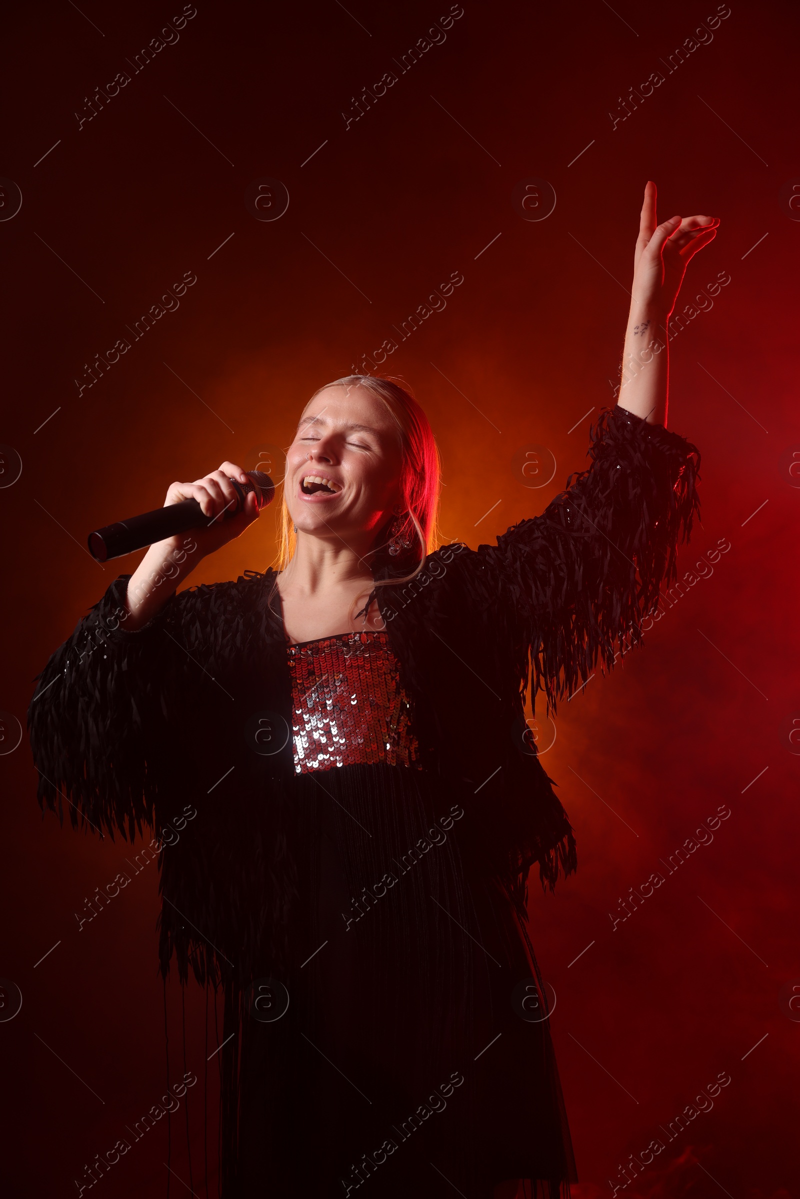 Photo of Beautiful singer performing on dark background with orange light