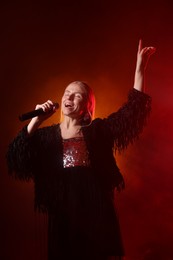 Beautiful singer performing on dark background with orange light